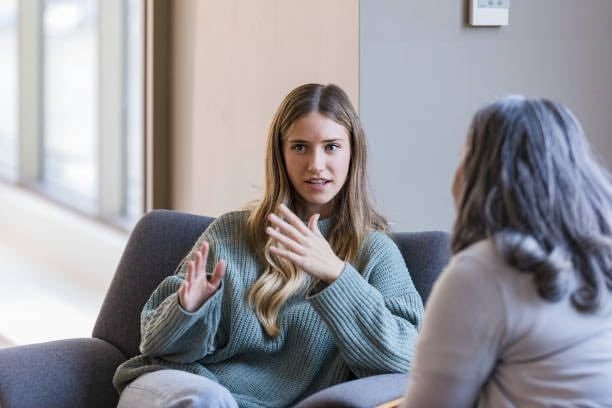 Individual Counselling Two women engaged in a discussion, sitting in a modern indoor setting.