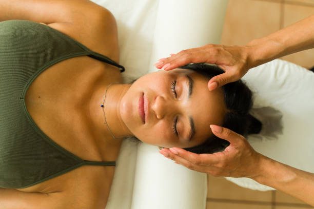 Reiki A woman receiving a facial massage while lying on a massage table.