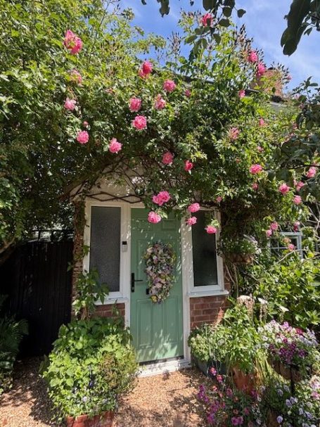 Mindful Moments Therapies Quaint green door framed by lush foliage and pink flowers.