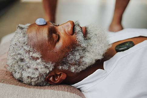 Pastlife regression An older man relaxes with stones placed on his forehead and chest.