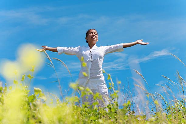 Somatic Resillience A woman with arms outstretched, enjoying the outdoors against a clear blue sky.