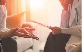Phiona Hutton Counsellor and Integrative therapist, in person Havant, Hampshire or online nationwide. A person in a white coat discussing with another person, sitting in a bright room.