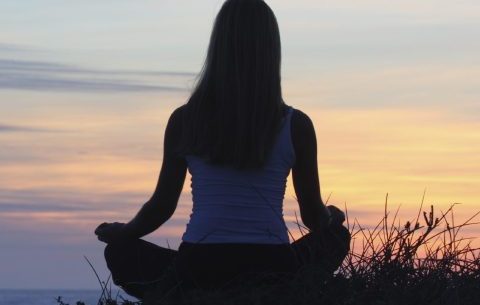 Phiona Hutton Counsellor and Integrative therapist, in person Havant, Hampshire or online nationwide. Person meditating on a hillside during a sunset, surrounded by grass.