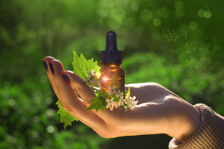 Flower remedies Brown glass dropper bottle on a hand, surrounded by leaves and small white flowers.